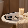 Heated bluetooth eye massager on a marble nightstand with a candle